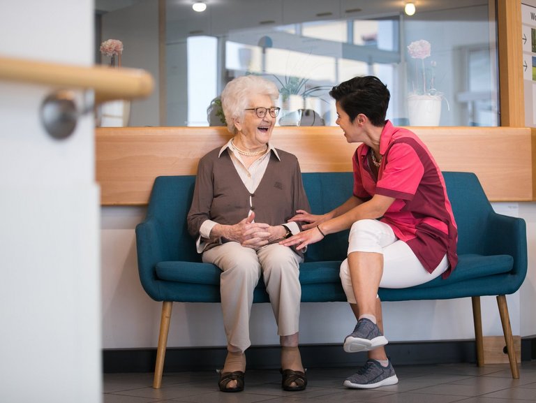 eine alte Frau sitzt lachend auf einer Bank - eine junge Frau lacht mit ihr