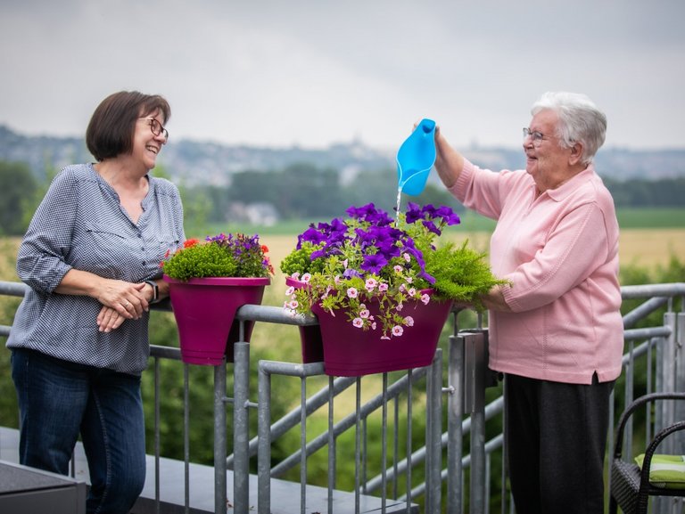 zwei Frauen am Balkon - eine gießt gerade Blumen