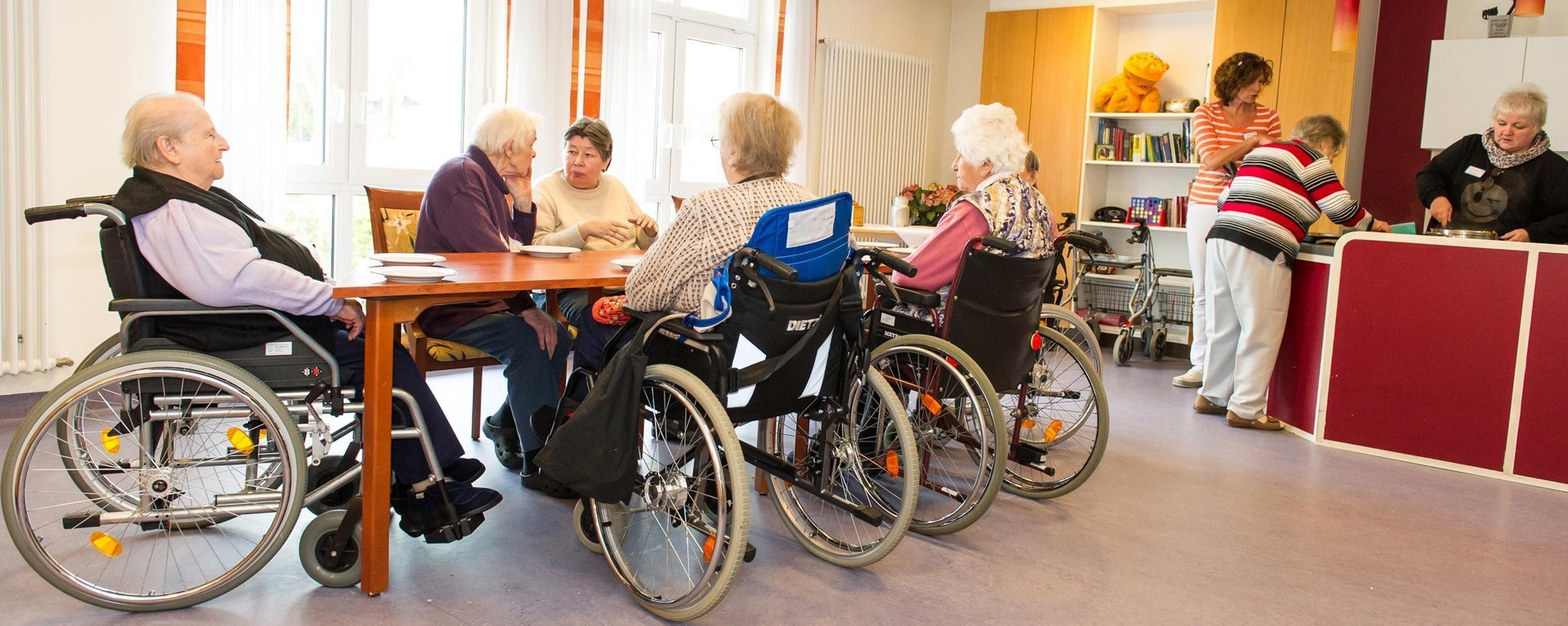 kurz vor dem Mittagessen - Eine Gruppe Bewohner wartet vor (noch) leeren Tellern