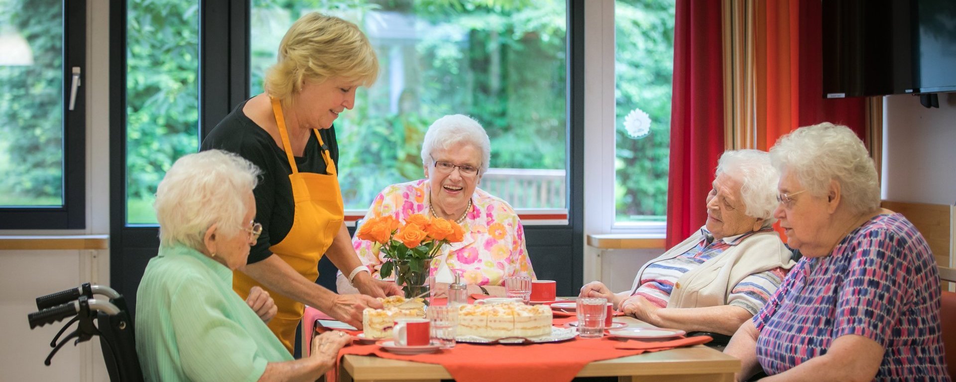 vier Frauen sitzen bei Kaffe und Kuchen welcher ihnen von einer jüngeren Frau serviert wird