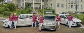 Pflegende stehen vor drei Autos des mobilen Pflegedienstes St. Elisabeth.